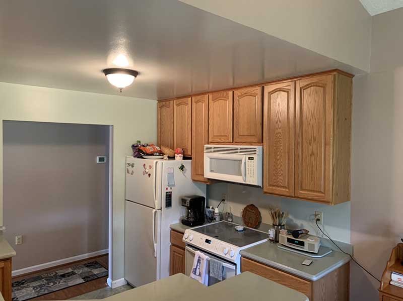 A dated kitchen with worn-out appliances, old-fashioned wooden cabinets, and faded wallpaper.