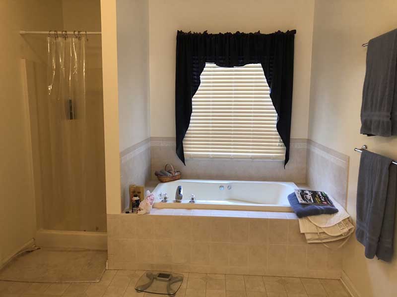 An old bathroom with yellowed tile, a cramped shower, and small bathtub.
