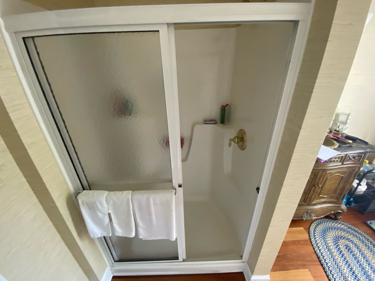 An old and cramped bathroom with limited storage, mismatched fixtures, and a cramped shower stall.