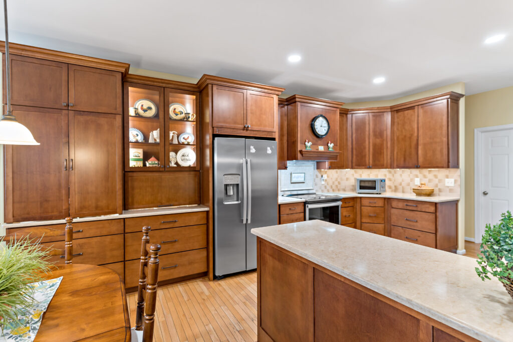 A spacious, modern kitchen featuring rich wooden cabinetry, granite countertops, stainless steel appliances, and a large island in a residential home.