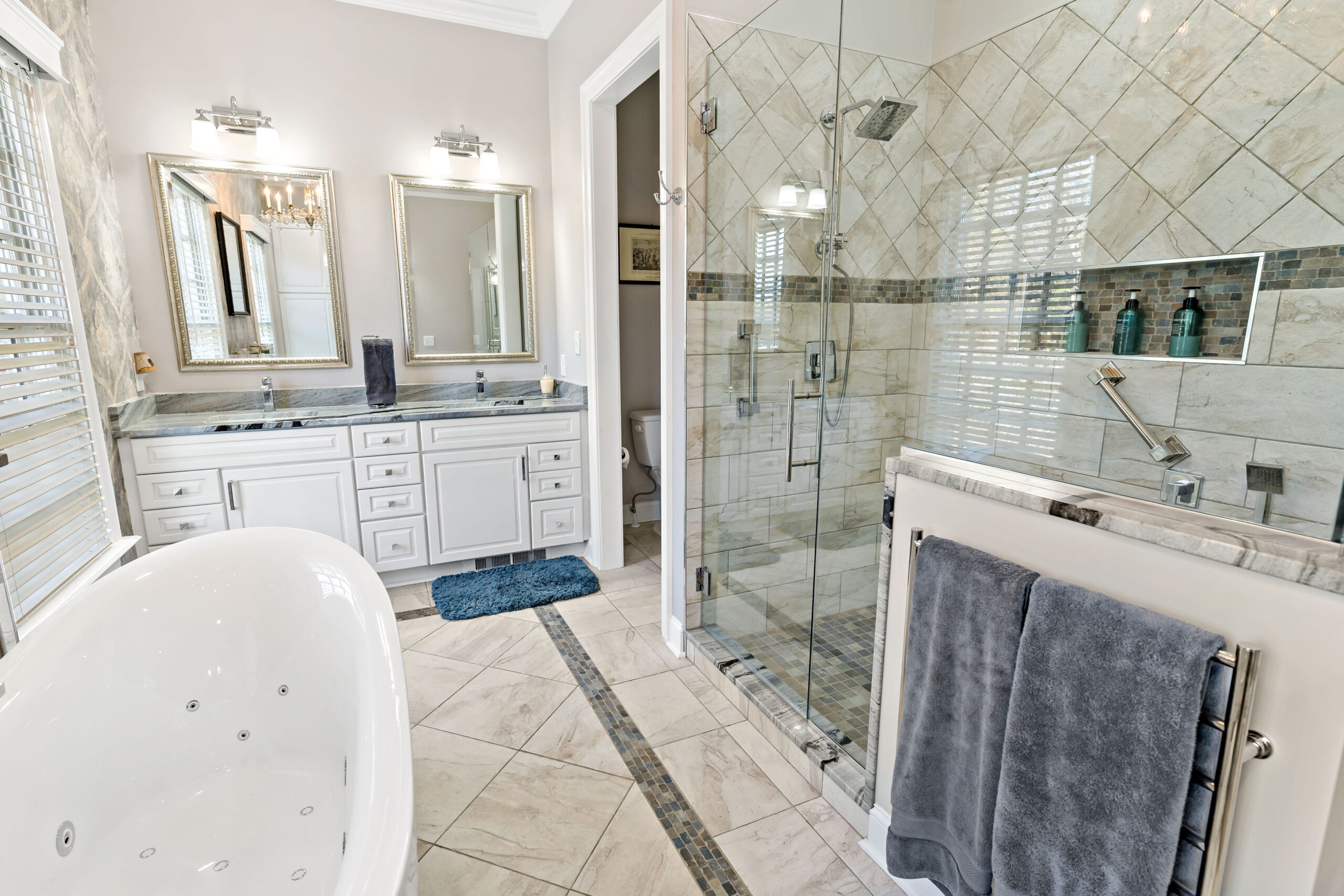 A luxurious modern bathroom features a white freestanding bathtub, large walk-in shower with glass enclosure, and dual vanity with mirrors under bright lighting.