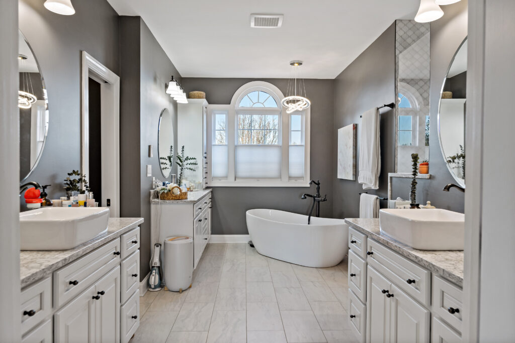 A luxurious modern bathroom featuring a freestanding soaking tub, dual vanities with mirrors, and abundant natural light from large windows.