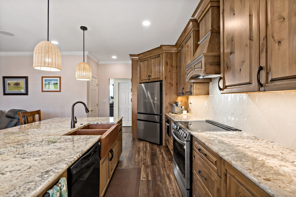 A spacious, modern kitchen features warm wood cabinetry, granite countertops, stainless steel appliances, and pendant lighting over a central island.
