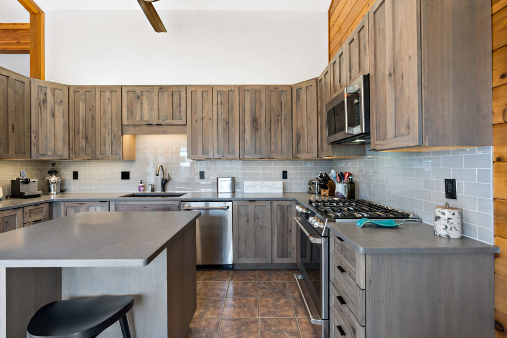 A modern kitchen with warm wooden cabinetry, stainless steel appliances, white subway tile backsplash, and an island with seating in a contemporary home.