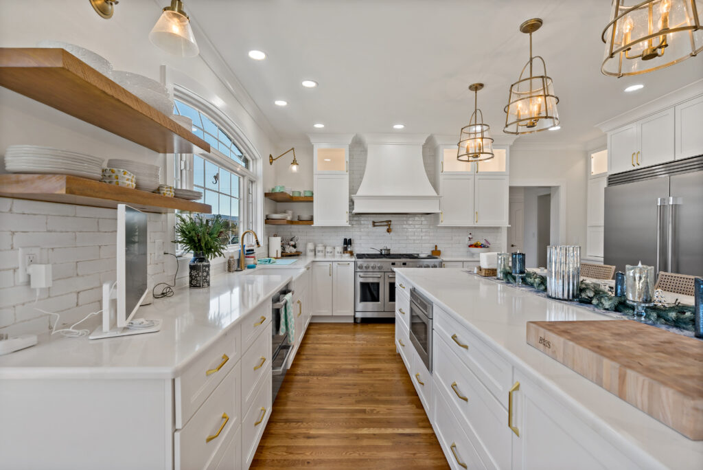 A bright, modern kitchen featuring white cabinetry, stainless steel appliances, warm wood tones, and elegant pendant lighting.