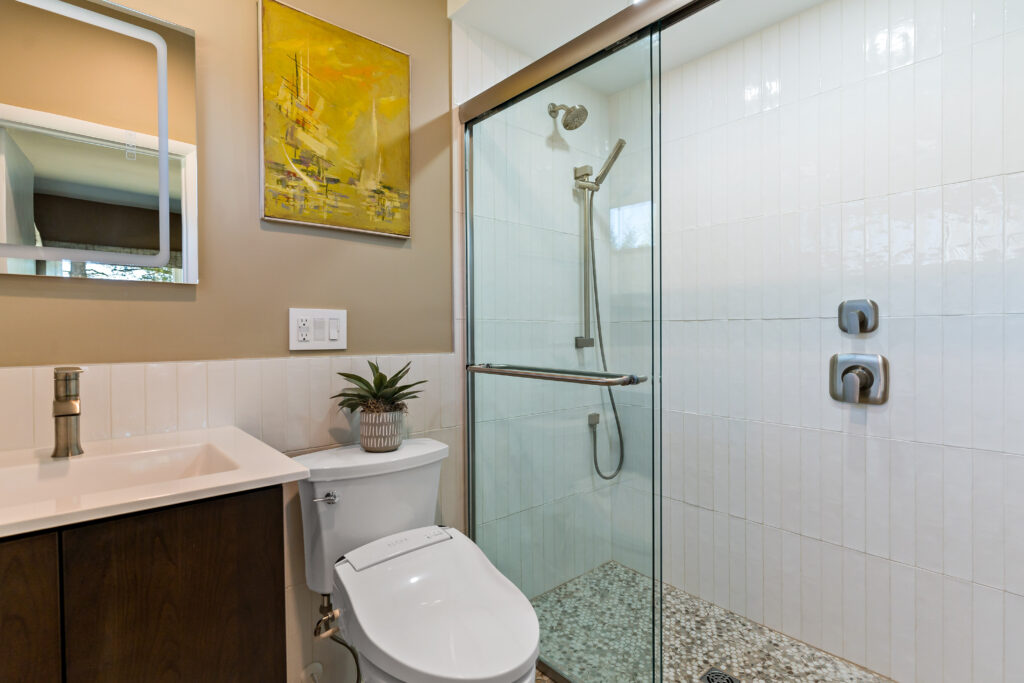 A contemporary bathroom with neutral tones features a dark wood vanity, white tile walls, glass shower enclosure, and modern fixtures.