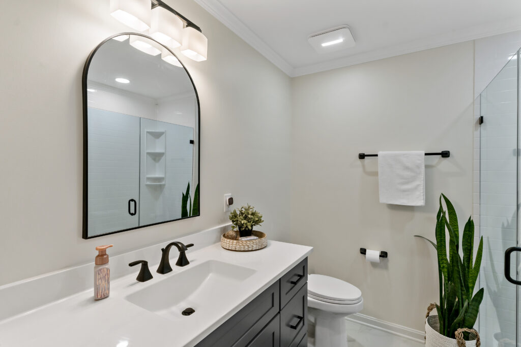 A modern, clean bathroom features a sleek vanity with an arched mirror, white ceramic sink, and contemporary fixtures alongside decorative elements.