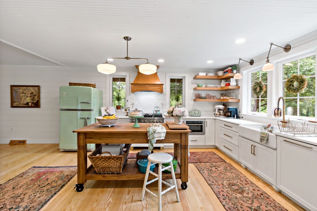 A bright, spacious modern kitchen with white cabinetry, wooden island, pendant lighting, and hardwood floors accentuated by a decorative area rug.