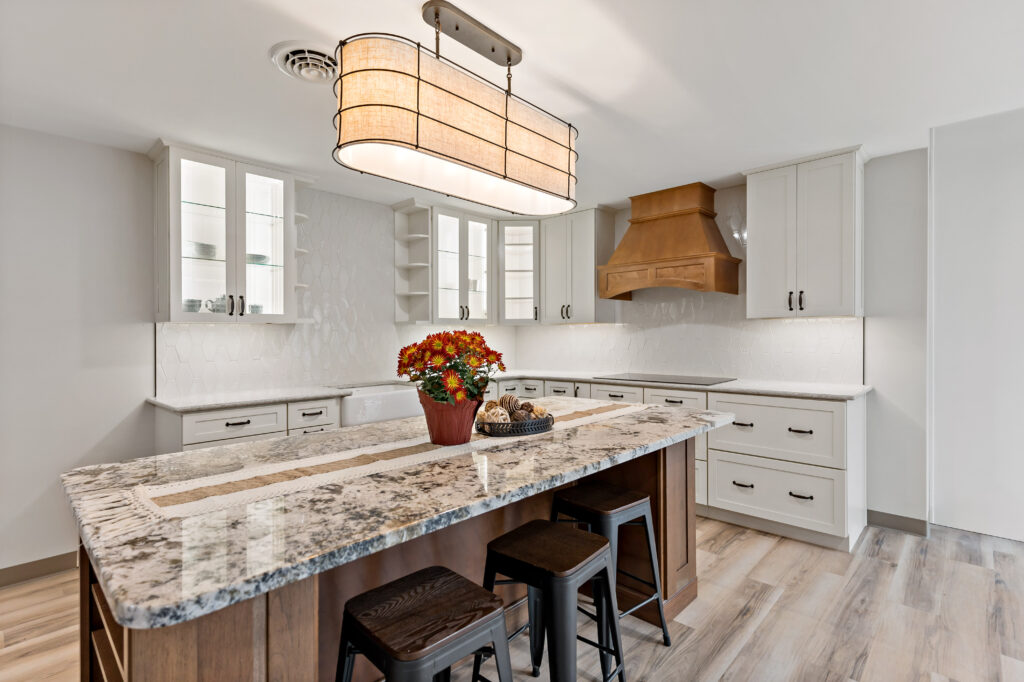 A bright, contemporary kitchen features white cabinetry, a multicolored granite island with seating, and warm lighting fixtures.