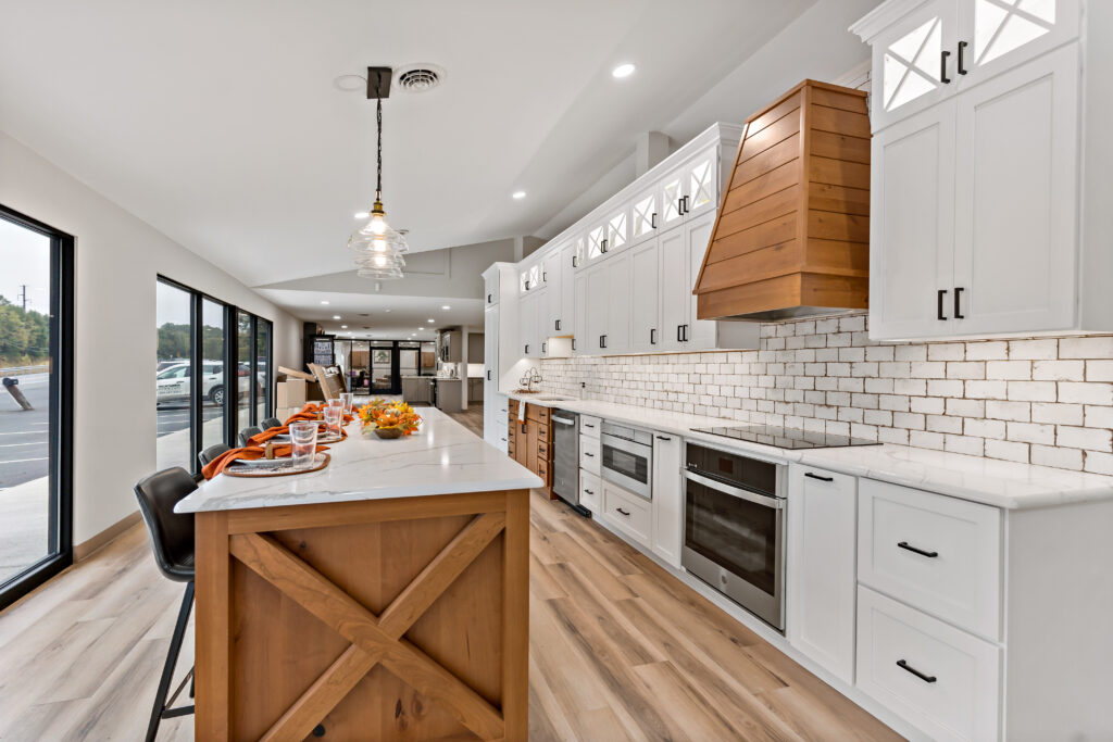 A modern kitchen with white cabinetry, wooden accents, and an island features subway tile backsplash and sleek stainless steel appliances under natural skylighting.
