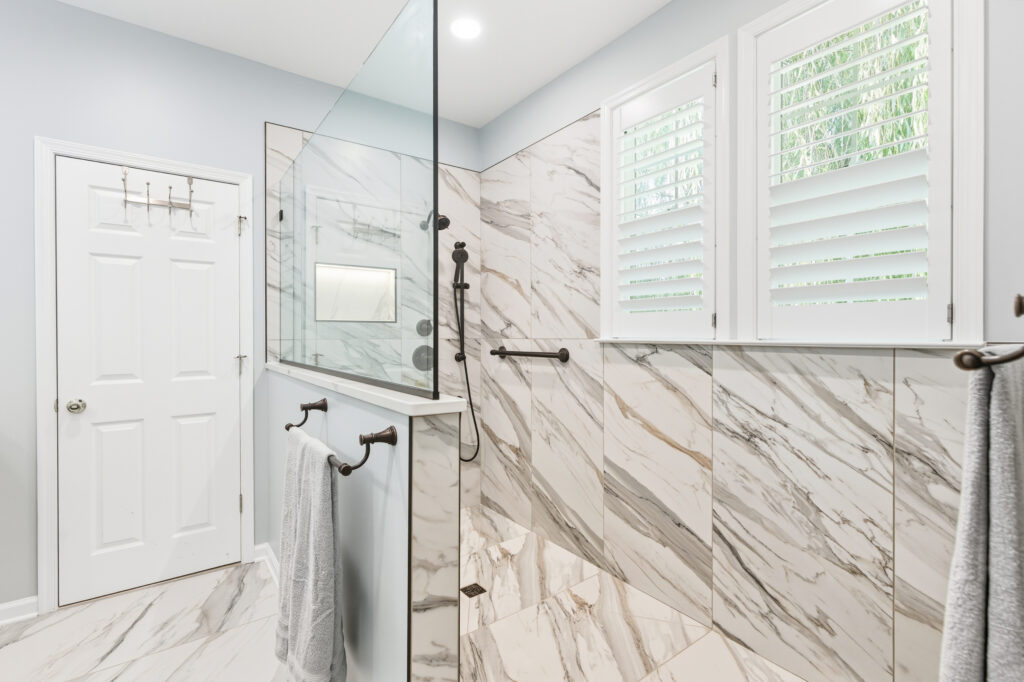 Glass-enclosed shower with marble-look tile and matte black fixtures