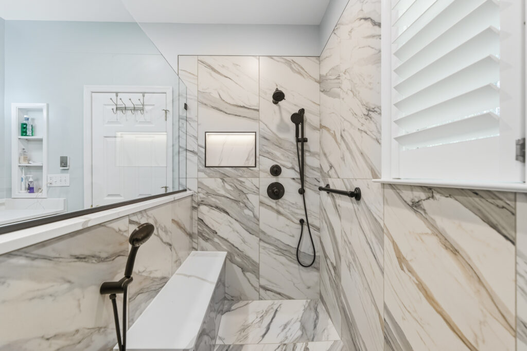 Marble-look tile shower with matte black fixtures and a built-in bench