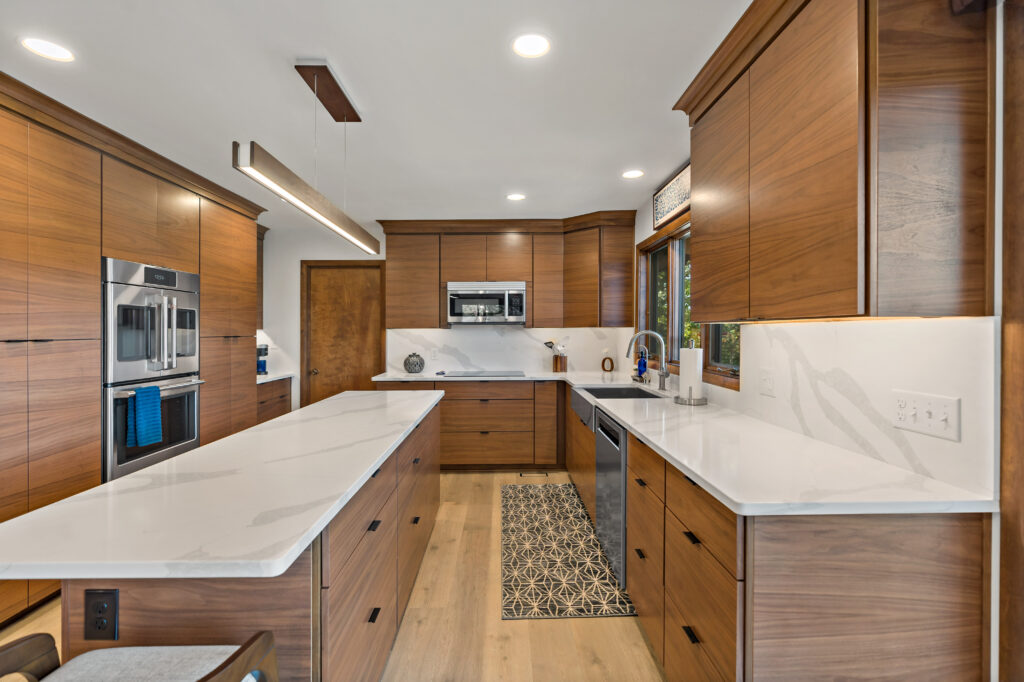 A contemporary kitchen featuring warm wood cabinetry, white quartz countertops, a central island, and high-end stainless steel appliances in a brightly lit open floor plan.