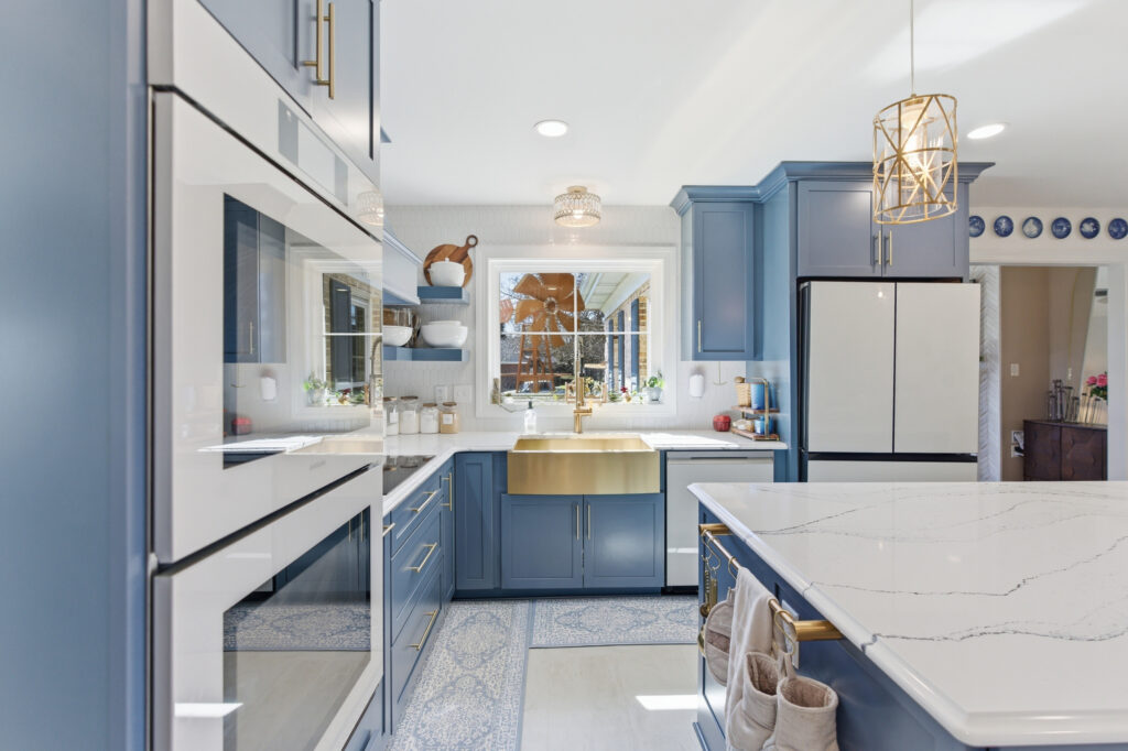 A contemporary kitchen features blue cabinetry, stainless steel appliances, marble countertops, and pendant lighting in a bright, clean interior space.