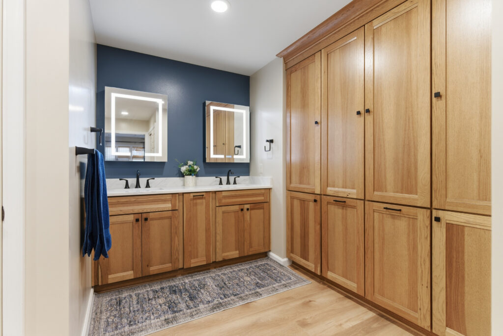 A modern bathroom interior featuring a wooden vanity with dual sinks, navy blue accent wall, and matching wooden cabinetry.