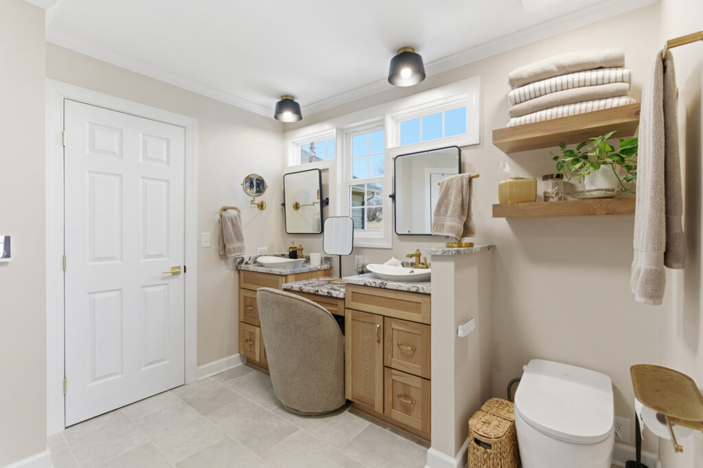 A bright, clean bathroom interior featuring a wooden vanity with dual sinks, storage cabinets, and organized shelving with towels and decorative elements.