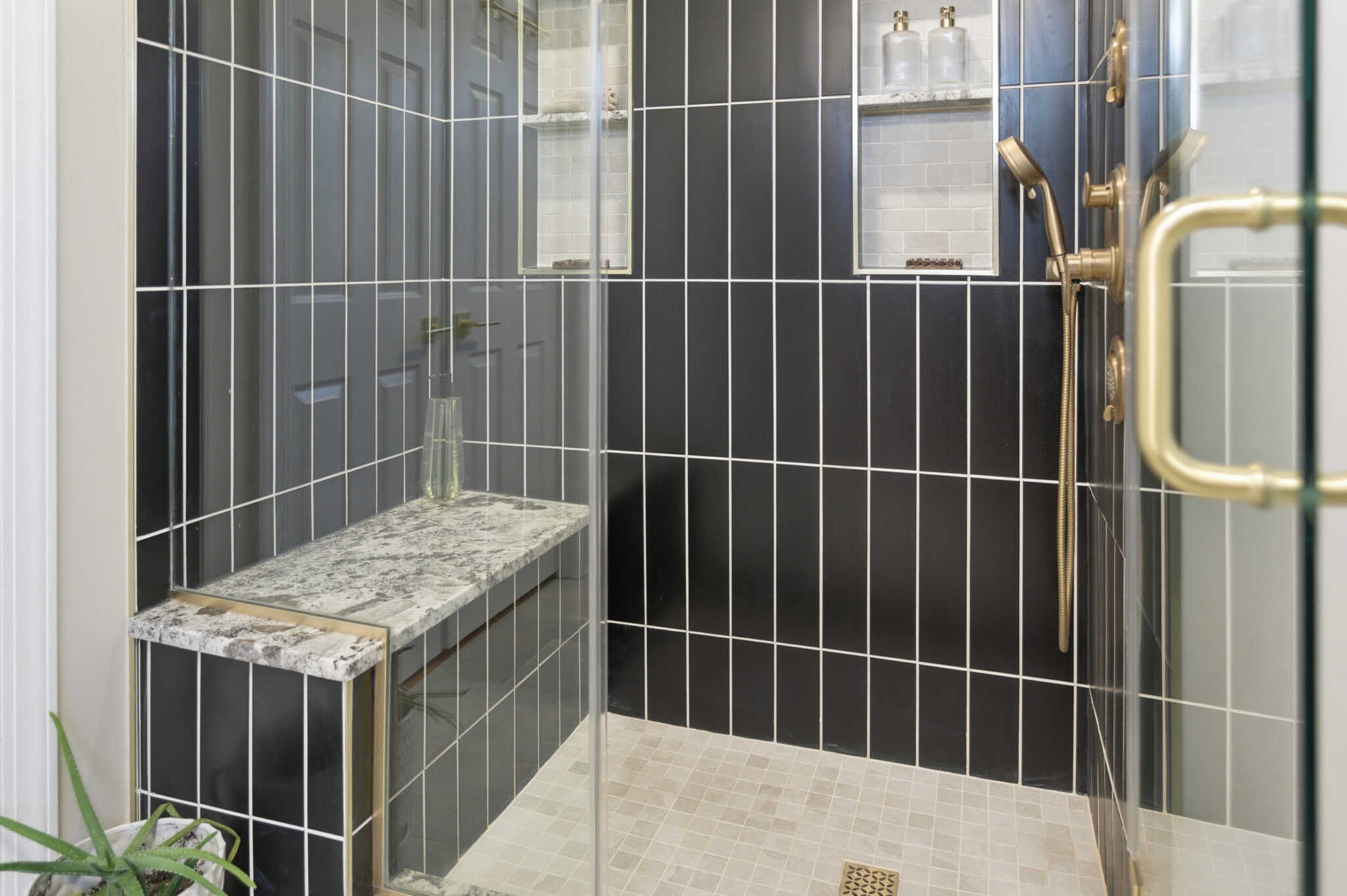 Walk-in shower with charcoal vertical tile, a stone bench and brass fixtures