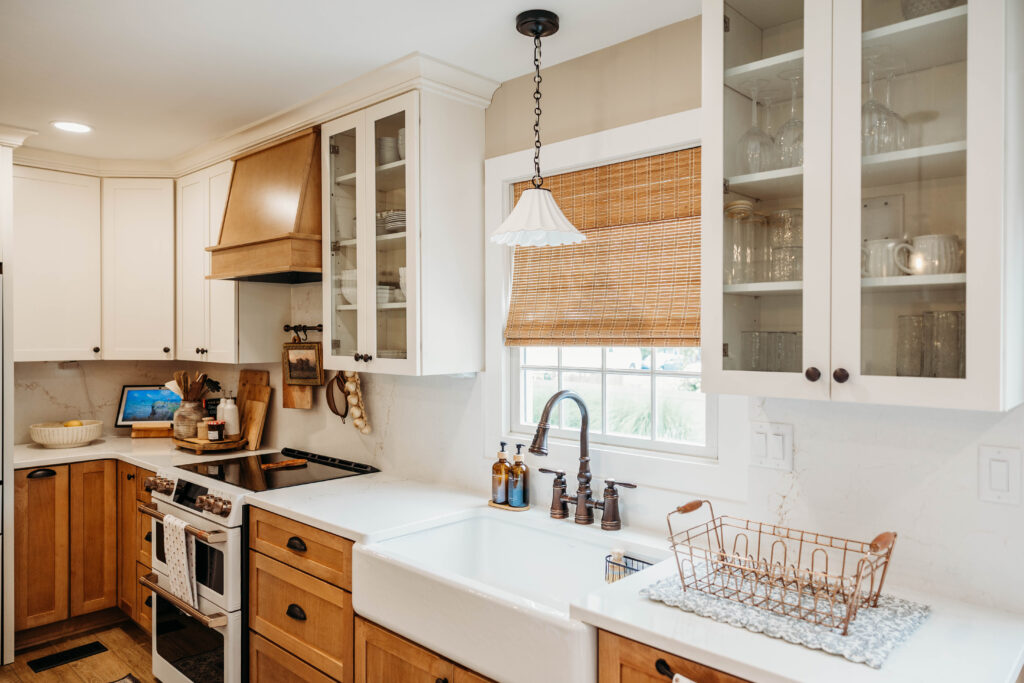 A bright, contemporary kitchen featuring mixed wood and white cabinetry, stainless steel appliances, and a farmhouse sink with pendant lighting.