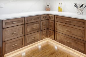 A modern kitchen corner featuring warm walnut cabinetry with a white marble countertop, stainless steel hardware, and organized cooking utensils in a bright, contemporary design.
