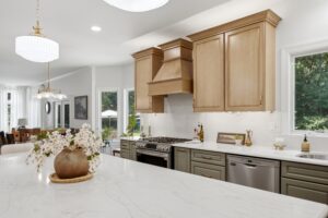 A bright, contemporary kitchen featuring natural wood cabinetry, a white marble island countertop, and modern pendant lighting in a well-lit residential space.