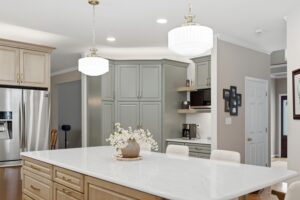 A contemporary kitchen features a white marble island with pendant lighting, gray cabinetry, and a mirrored backsplash in a bright, open layout.