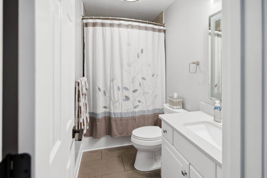 A clean, modern bathroom featuring a floral shower curtain, white toilet, and vanity sink with mirror.
