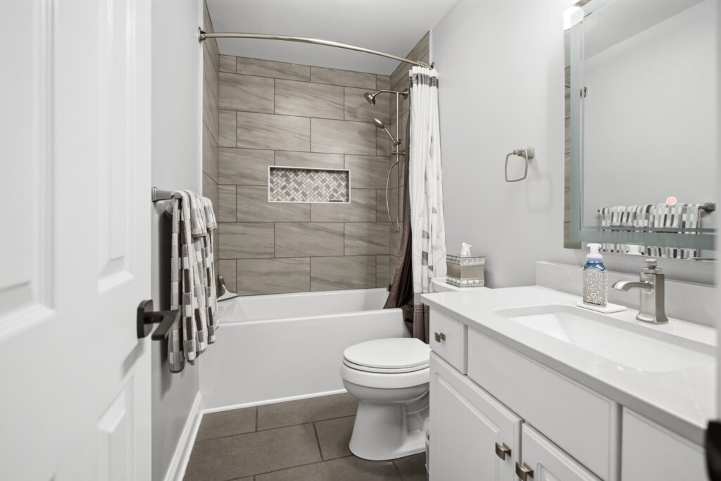 A modern bathroom featuring a tiled tub-shower combo, white toilet, and white vanity with sink.