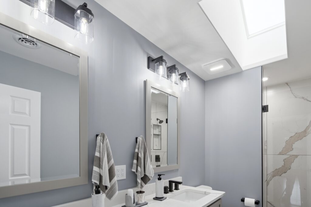 A modern bathroom with a vanity, mirrors, black fixture lighting, striped towels, and a skylight illuminating the space.