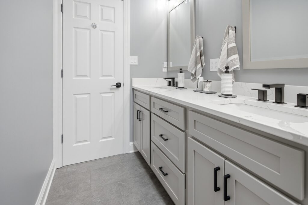 A modern bathroom featuring a white double-sink vanity with marble countertop, black fixtures, striped towels, and a white paneled door.