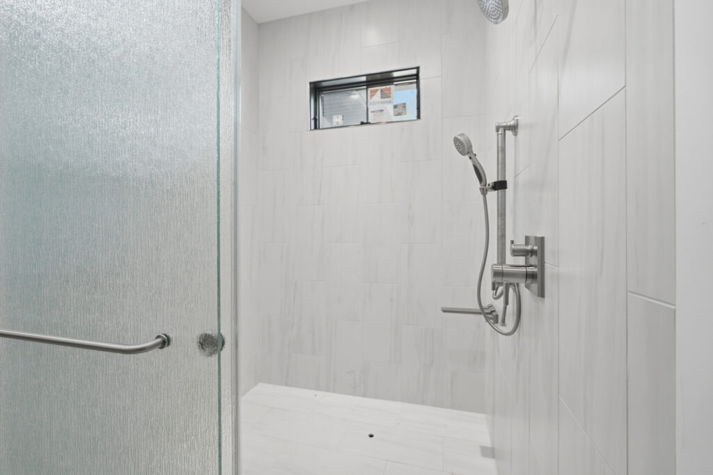 A modern tiled walk-in shower with a glass door, dual showerheads, and a small window.